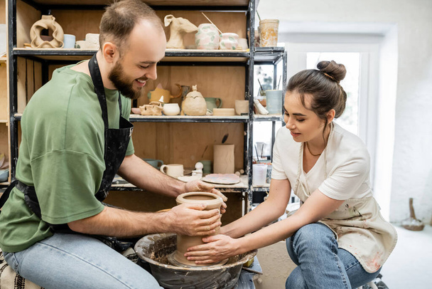 Positieve paar pottenbakkers vormgeven klei vaas op aardewerk wiel samen in keramische studio - Foto, afbeelding