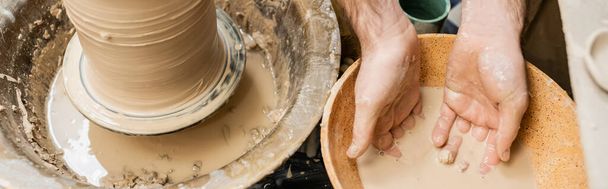 Vista superior do artesão trabalhando com água na tigela perto de argila e roda de cerâmica no estúdio de cerâmica, banner - Foto, Imagem