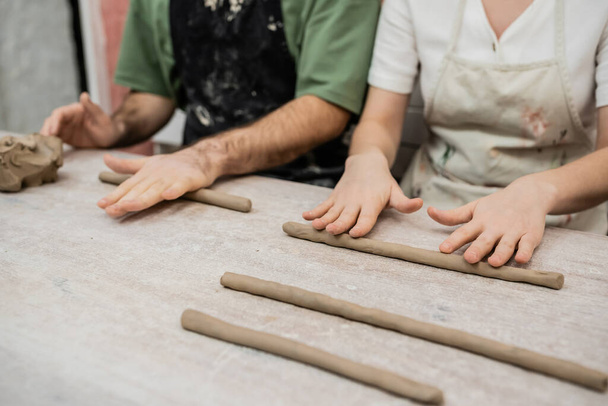 Vista recortada de un borroso par de artesanos moldeando arcilla en la mesa mientras trabajan en taller de cerámica - Foto, imagen