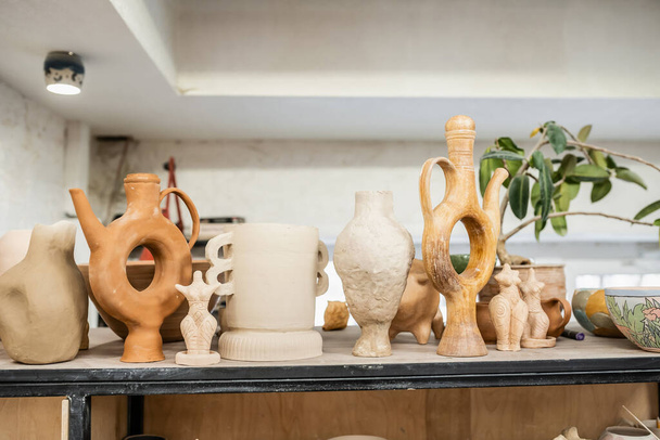 Фигуры из глины и скульптуры на стойке в размытой керамической мастерской - Фото, изображение