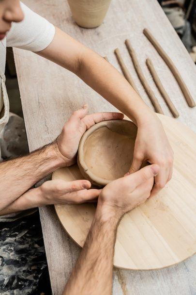 Top view of romantic couple shaping clay bowl together in ceramic workshop - Фото, зображення