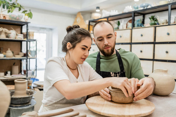 Brunette craftswoman in apron making clay bowl with boyfriend together in ceramic workshop - Photo, Image