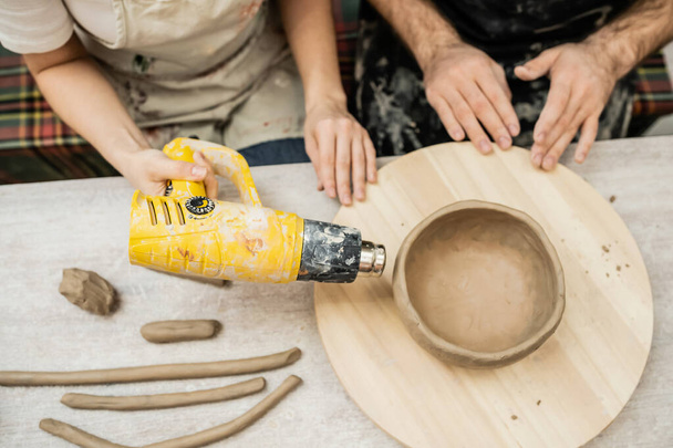 研修会の木板の熱銃が付いている粘土ボールを乾燥する陶器のカップルのトップビュー - 写真・画像