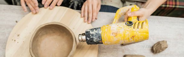 Draufsicht der Kunsthandwerker beim Trocknen von Ton-Töpferwaren mit Heißluftpistole an Bord in der Keramikwerkstatt, Banner - Foto, Bild