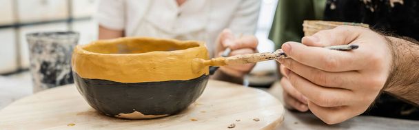 Uśmiechający się garncarze w fartuchy kolorowanki ceramiczne miski na drewnianej desce w studio ceramiki na tle - Zdjęcie, obraz