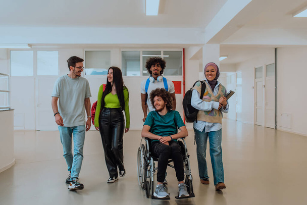 In a modern university, a diverse group of students, including an Afro-American student and a hijab-wearing woman, walk together in the hallway, accompanied by their wheelchair-bound colleague - Photo, Image
