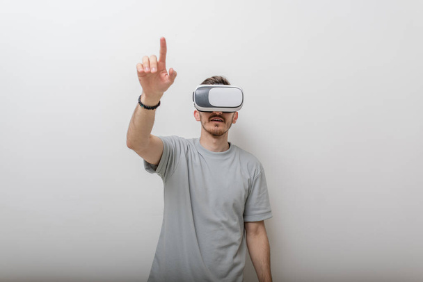 Futuristischer Mann mit Virtual-Reality-Brille interagiert mit der Luft in einem isolierten grauen Hintergrund. Hochwertiges Foto - Foto, Bild