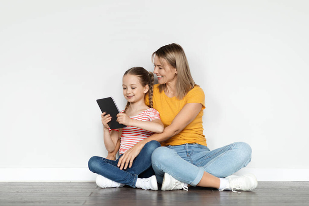 Nice App. Портрет улыбающейся молодой матери и маленькой дочери с помощью цифрового планшета вместе дома, белая мама и симпатичная женщина ребенок расслабляется на полу с современным гаджетом, скопировать пространство - Фото, изображение