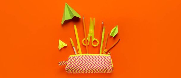 Paper planes with pencil case and school supplies on orange background - Photo, Image
