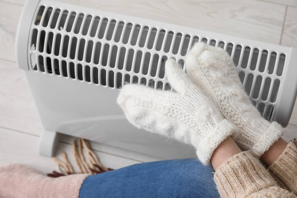 Woman warming hands in mittens near radiator at home, closeup - Foto, afbeelding