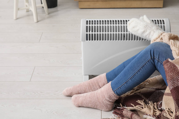 Woman in winter clothes warming near radiator at home, closeup - Foto, Imagem