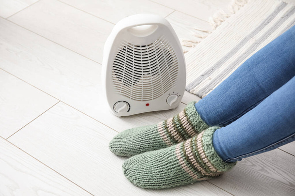 Nő melegítő lábak zokni közelében elektromos ventilátor melegítő otthon, közelkép - Fotó, kép