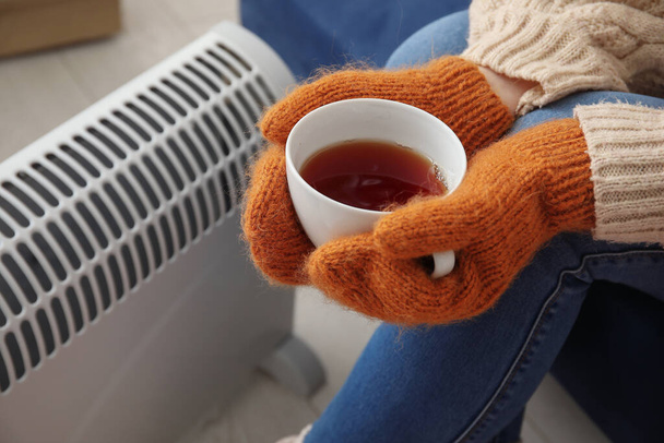 Kobieta z filiżanką gorącej kawy ocieplenie w pobliżu chłodnicy w domu, zbliżenie - Zdjęcie, obraz