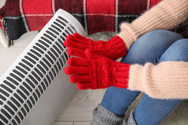 Mujer calentando las manos en guantes cerca del radiador en casa, primer plano - Foto, Imagen