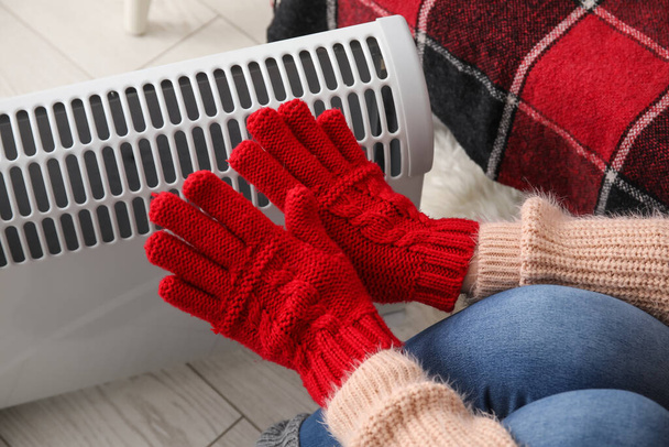 Woman warming hands in gloves near radiator at home, closeup - Photo, Image