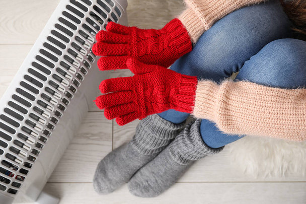 Mujer calentando las manos en guantes cerca del radiador en casa, primer plano - Foto, Imagen