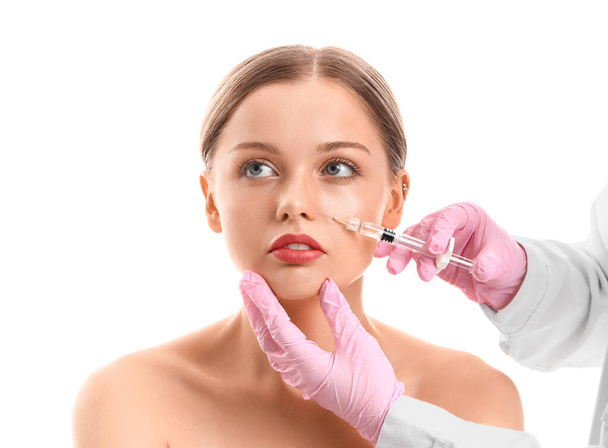 Mujer joven recibiendo inyección de relleno en la cara contra fondo blanco - Foto, Imagen