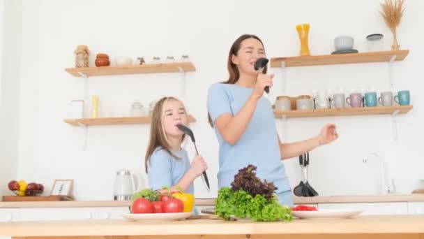 Äiti ja tytär laulavat lusikoilla kotona keittiössä. Onnellinen perhe ruoanlaitto yhdessä keittiössä - Materiaali, video