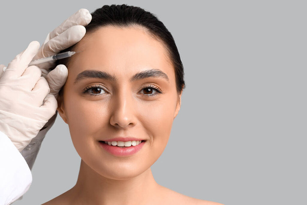 Young woman receiving filler injection in face against grey background - Φωτογραφία, εικόνα