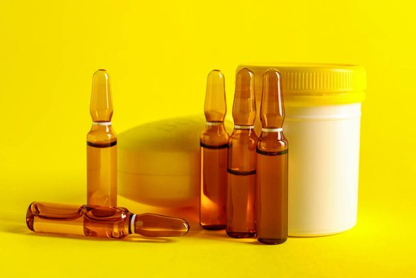 Ampules and jar with pills on yellow background - Photo, Image