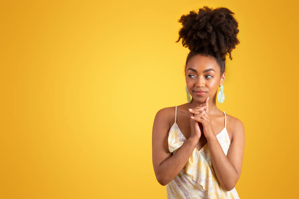 Thoughtful smiling millennial african american lady in dress thinking, looking at empty space, isolated on yellow background, studio. Choice of fashion lifestyle, people emotions, ad and offer - Фото, зображення