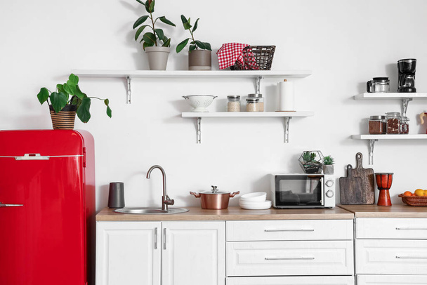 Interieur van lichte keuken met rode koelkast, aanrecht, planken en kamerplanten - Foto, afbeelding