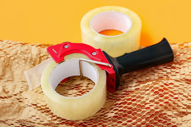 Adhesive tape roll, dispenser and paper on orange background - Foto, imagen