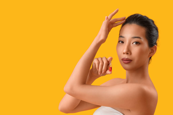 Beautiful Asian woman with ampule on yellow background. Skin care concept - Photo, Image