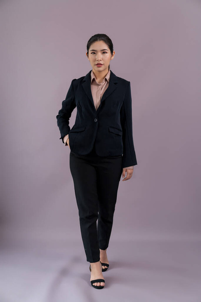 Full body length image of confident young businesswoman stands on isolated background, posing in formal black suit. Office lady or manager with smart and professional appearance. Enthusiastic - 写真・画像