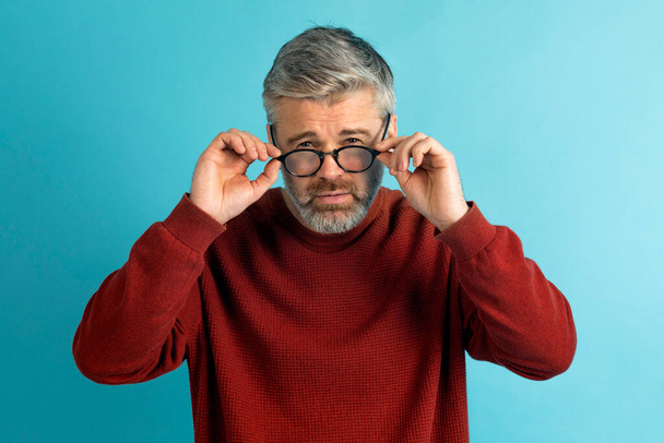 Mann mittleren Alters hält seine Brille zur Kontrolle, weil sie den Fokus nicht mit seinem Sehvermögen auf blau anpasst. Gesundheitsproblem der Sehkraft. Optometrie. Gläser mit konvexen oder konkaven Linsen. Kurzsichtigkeit. Augenkrankheit. - Foto, Bild