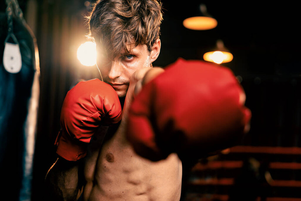 Boxing fighter shirtless posing, caucasian boxer punch his fist in front of camera in aggressive stance and ready to fight at gym with kicking bag and boxing equipment in background. Impetus - Foto, Bild
