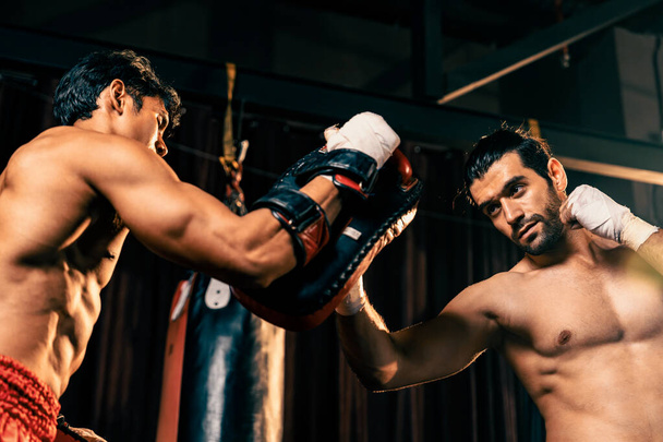 Le boxeur asiatique et caucasien Muay Thai déclenche une attaque de poinçon de coupe supérieure dans une séance d'entraînement de boxe féroce, livre une frappe de poinçon à l'entraîneur sparring, mettant en valeur la technique et les compétences de boxe thaïlandaise Muay. Impulsion - Photo, image