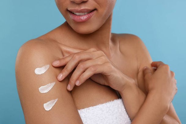 Young woman applying body cream onto arm on light blue background, closeup - Foto, afbeelding