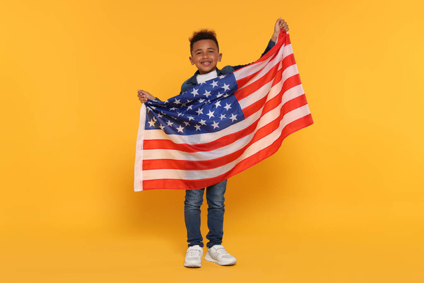 4 lipca - Dzień Niepodległości USA. Szczęśliwy chłopiec z amerykańską flagą na żółtym tle - Zdjęcie, obraz