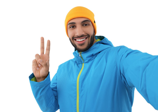 Smiling young man taking selfie and showing peace sign on white background - Fotoğraf, Görsel