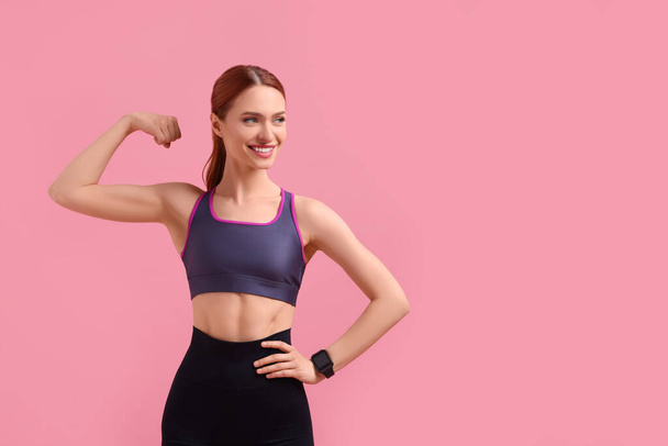 Young woman in sportswear showing muscles on pink background, space for text - Photo, image
