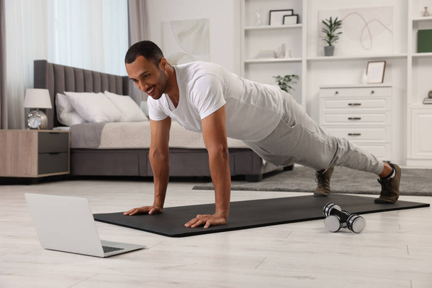 Man doing morning exercise on fitness mat near laptop at home - Foto, afbeelding