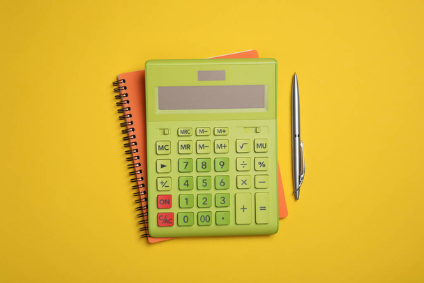 Calculator, notebook and pen on yellow background, flat lay - Φωτογραφία, εικόνα