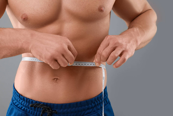 Athletic man measuring waist with tape on grey background, closeup. Weight loss concept - Valokuva, kuva