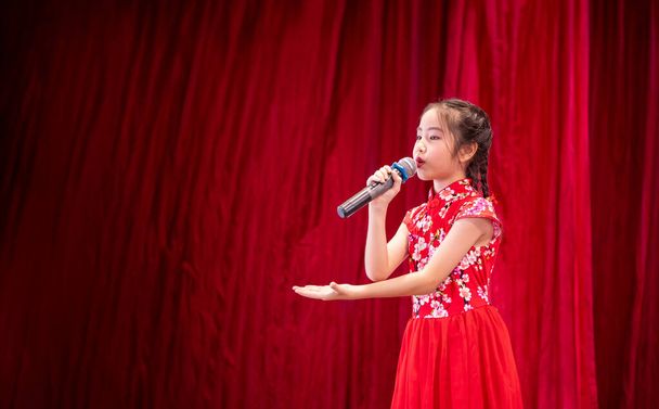 The Asian kid girl sing a song on stage at her school activity day, dress in Qipao style, red curtain background - Fotografie, Obrázek