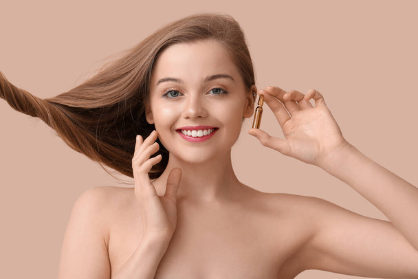 Beautiful young woman with ampule on beige background. Hair loss treatment - Photo, Image