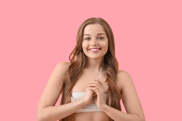 Красива молода жінка з ампулом на рожевому фоні. Концепція догляду за шкірою - Фото, зображення
