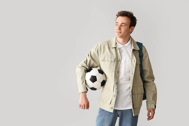 Αντρας μαθητής με σακίδιο και μπάλα ποδοσφαίρου σε γκρι φόντο - Φωτογραφία, εικόνα