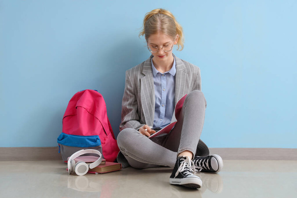 Female student with backpack and headphones sitting near blue wall - Фото, зображення