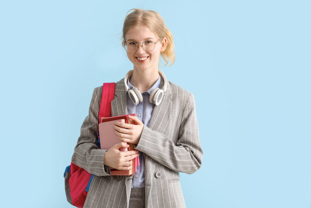Šťastná studentka s batohem, knihami a sluchátky na modrém pozadí - Fotografie, Obrázek
