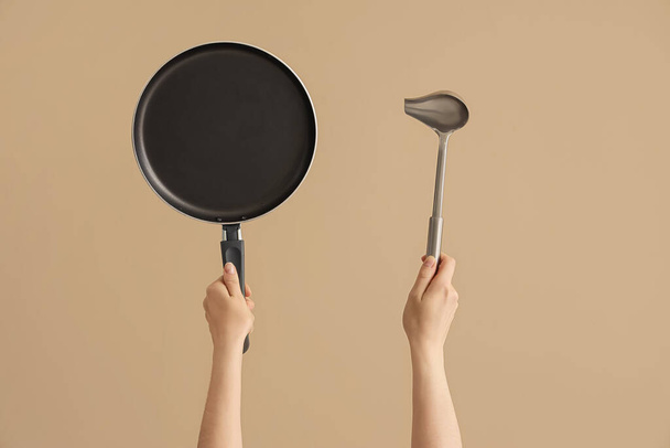 Female hands holding frying pan and ladle on brown background - Photo, image