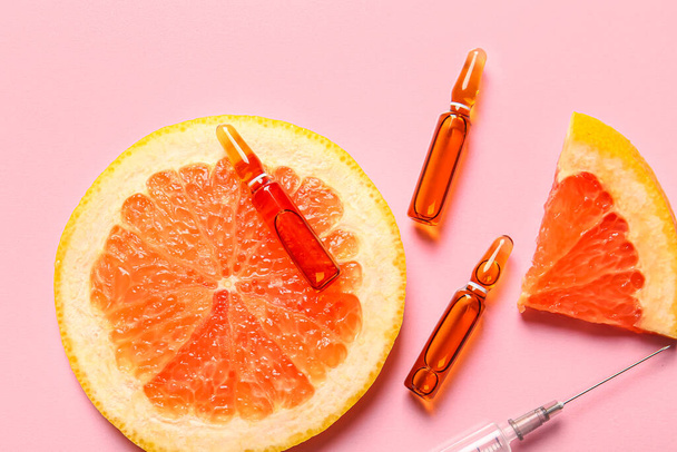 Ampollas con vitamina C y rodajas de pomelo sobre fondo rosa - Foto, imagen