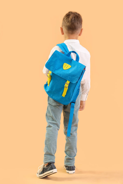 Little schoolboy with blue backpack on orange background, back view - Photo, Image