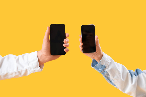 Νεαρό ζευγάρι με κινητά τηλέφωνα σε κίτρινο φόντο - Φωτογραφία, εικόνα