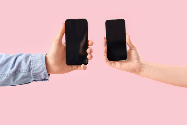 Νεαρό ζευγάρι με κινητά τηλέφωνα σε ροζ φόντο - Φωτογραφία, εικόνα